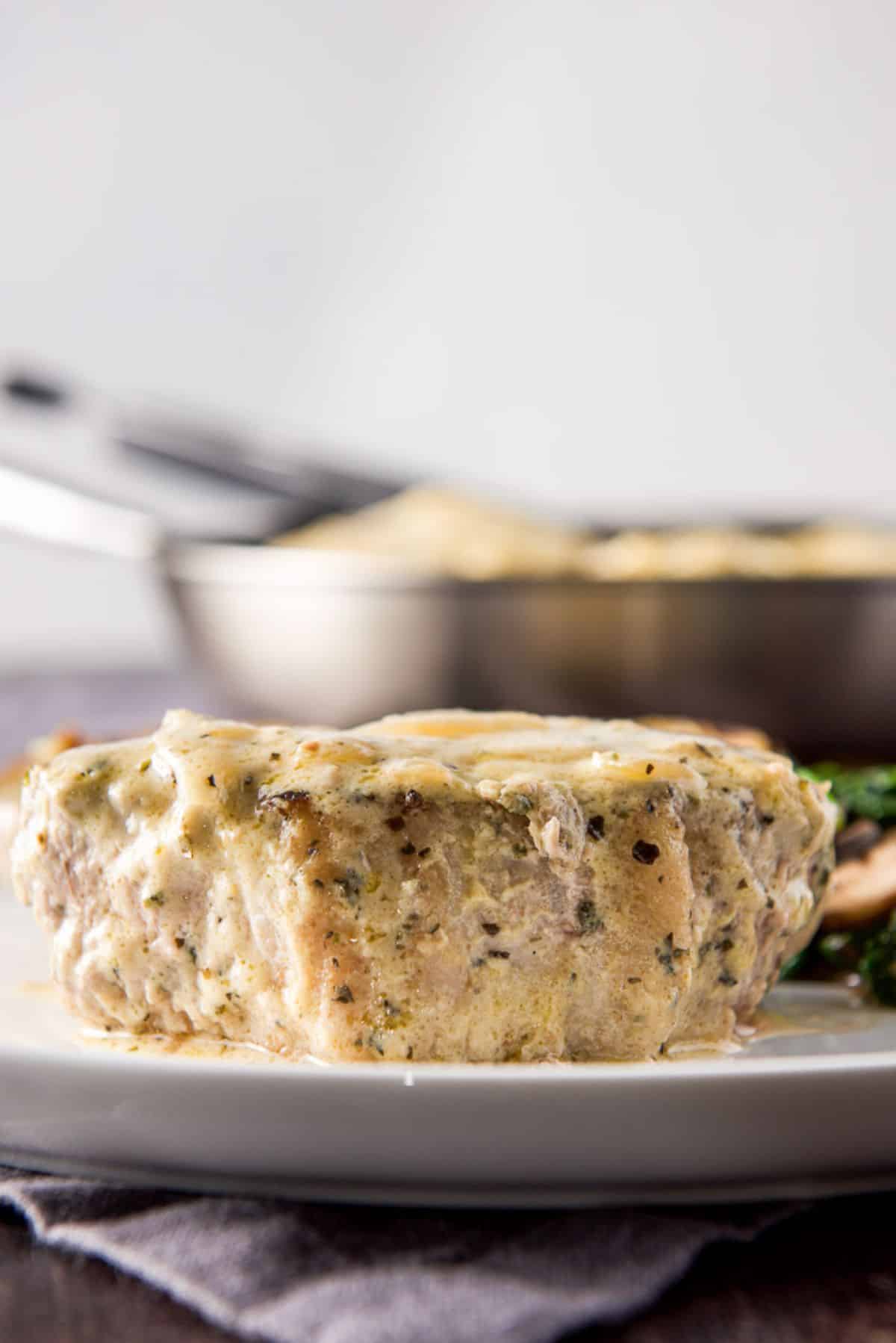 Vertical view of a pork chop on a plate with the pan in the background