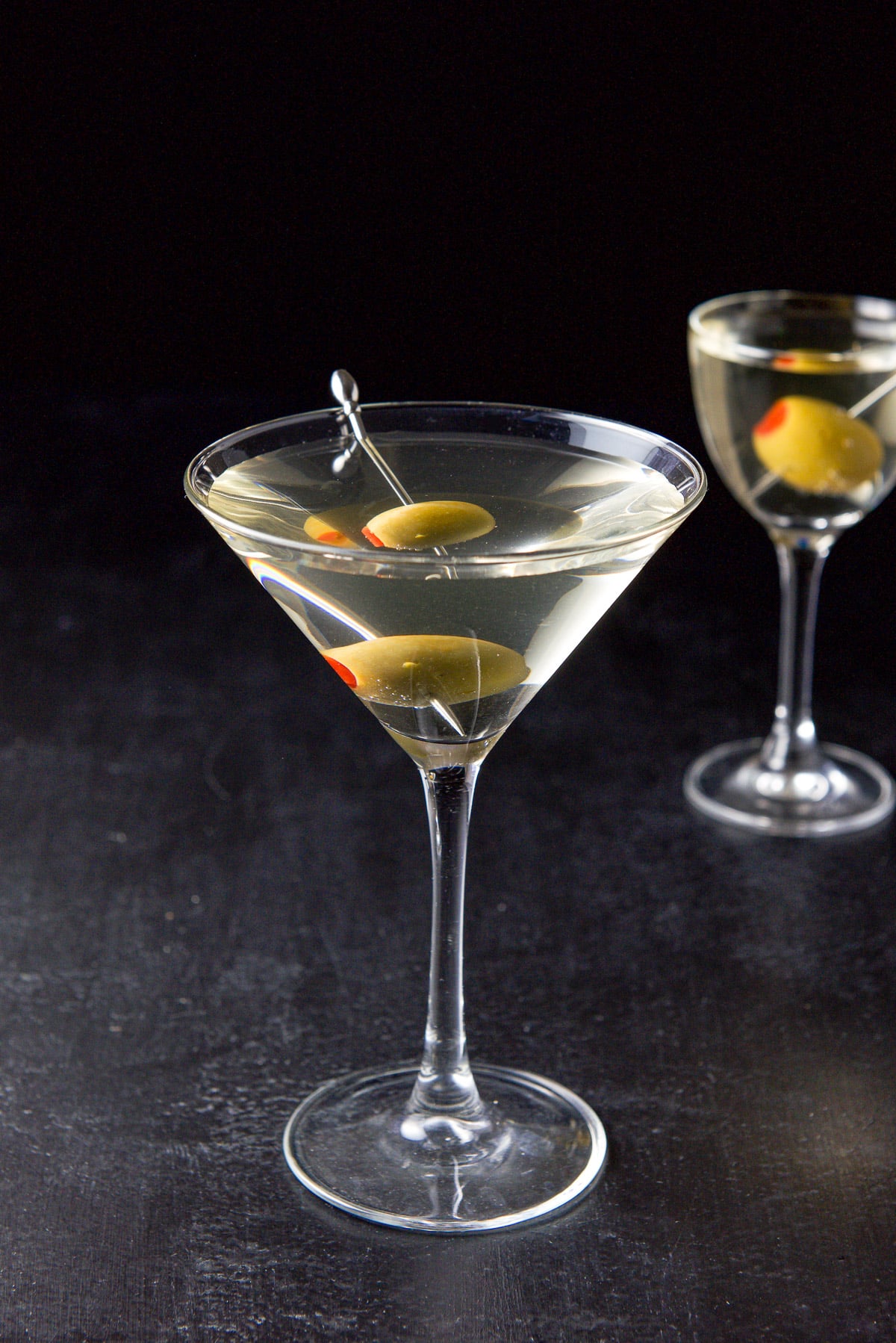 Two martini glasses filled with the martini with olives on picks as garnish
