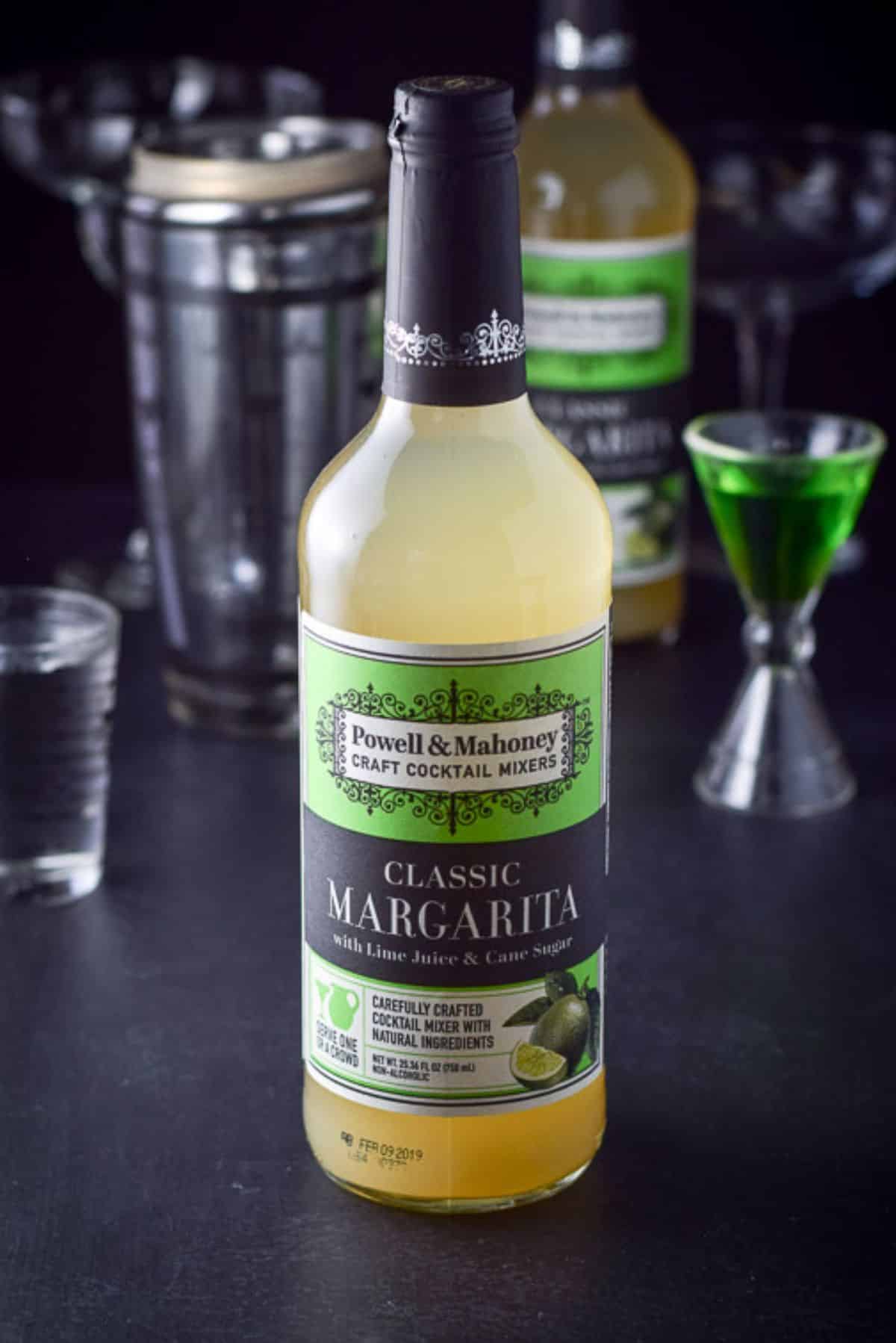 A bottle of margarita mix along with some melon liquor and tequila