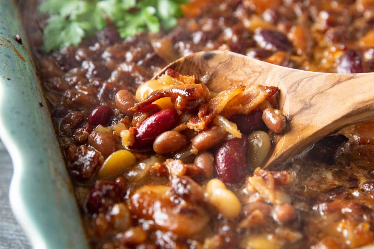 a wooden spoon in a dish of baked beans