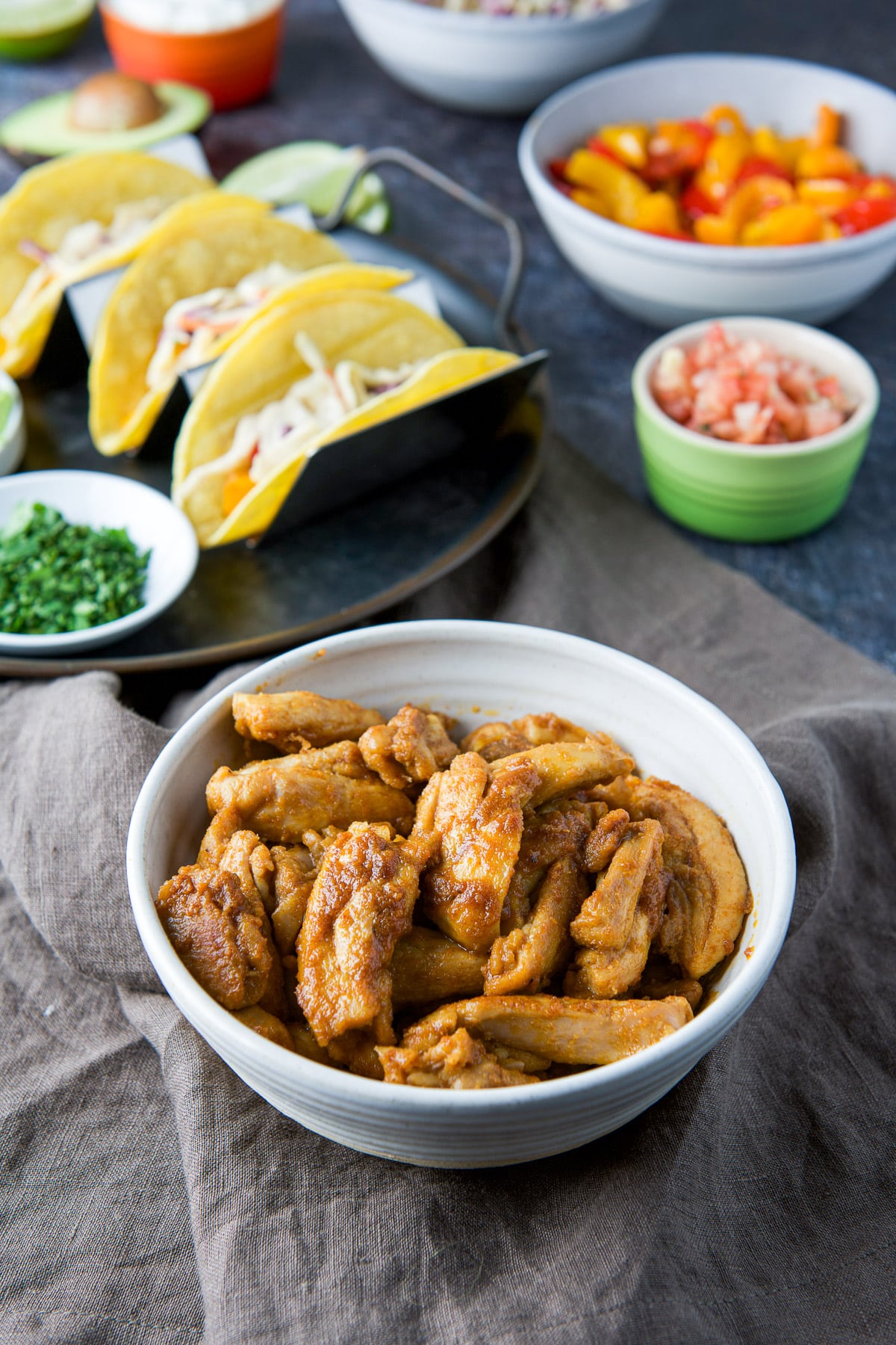 A small bowl with the cooked chicken strips in front of the taco shells and other addons for the tacos