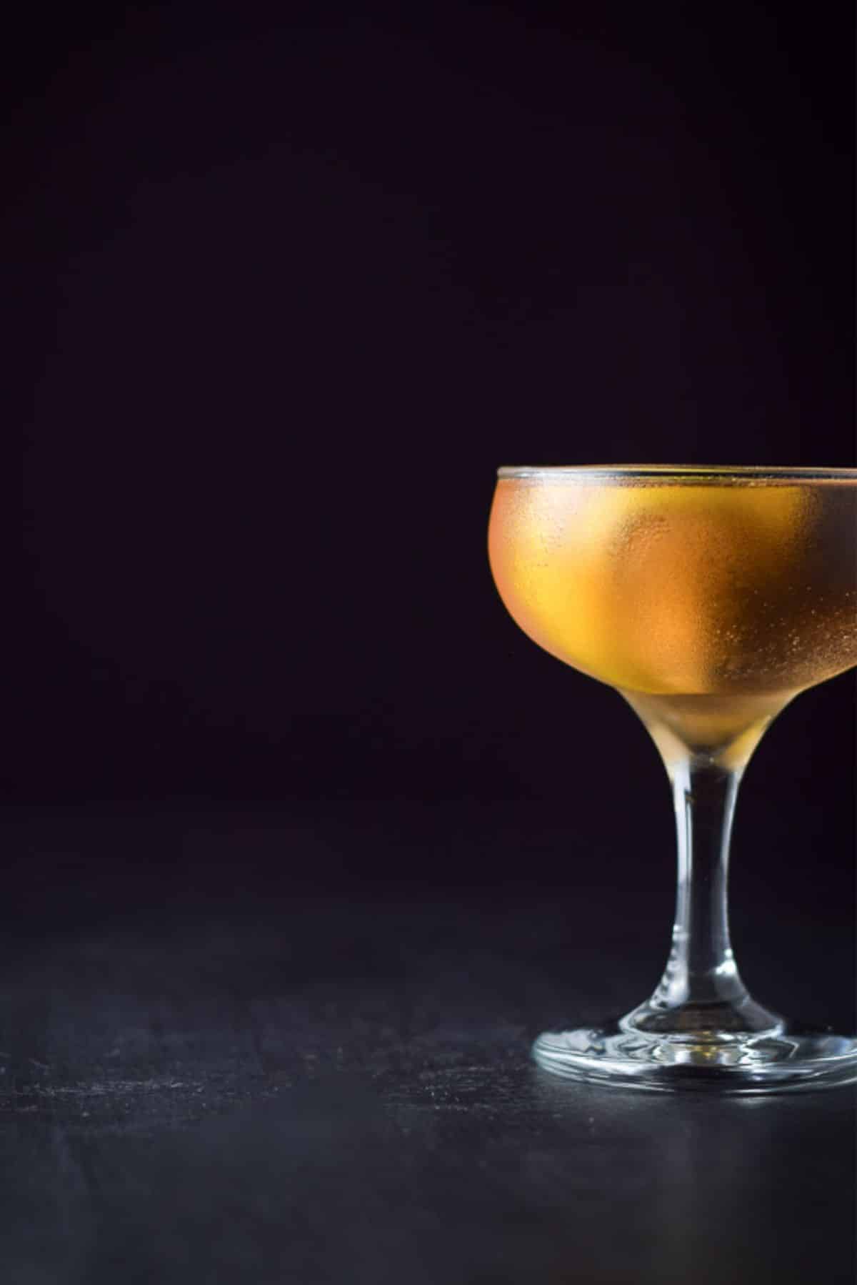 The amber cocktail in a coupe glass with it half out of the photo