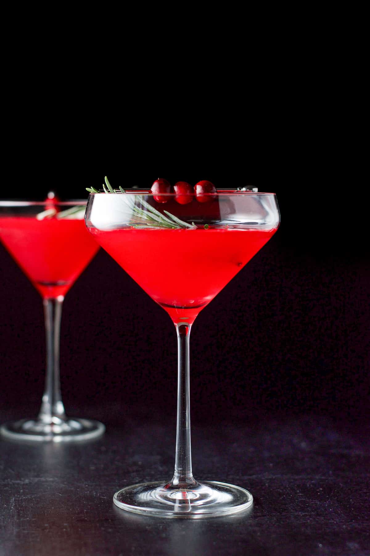 Vertical view of the cosmo with cranberries and rosemary as garnish
