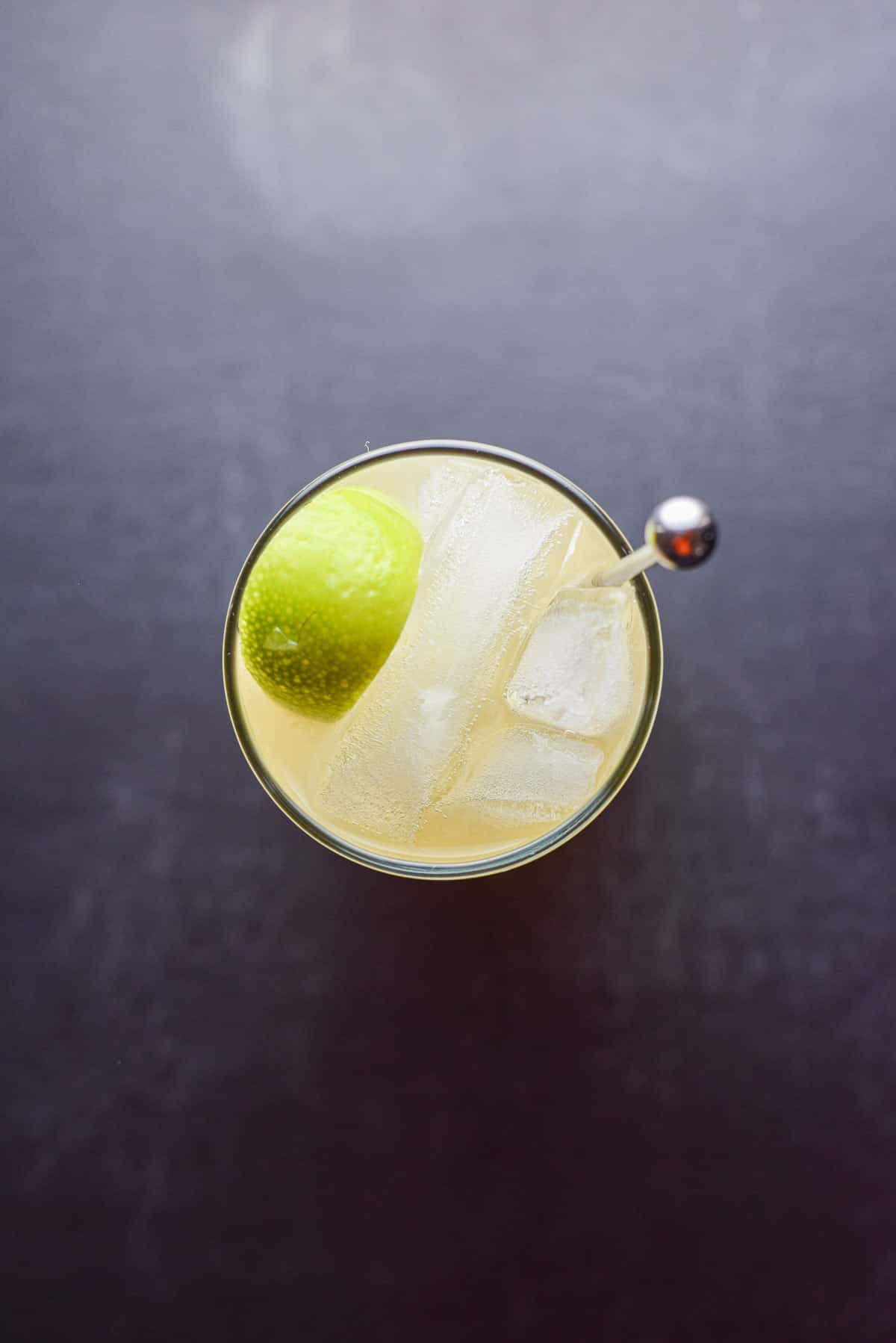 Overhead view of the glass with the stirrer, ice and lime wedge