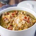 A square photo of chicken, broth, vegetables and broth in a white pan