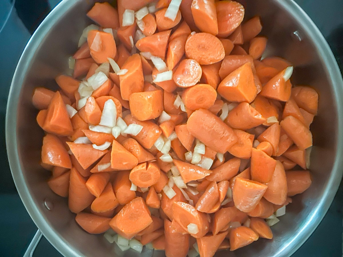 Carrots and onions tossed in oil in a metal pan