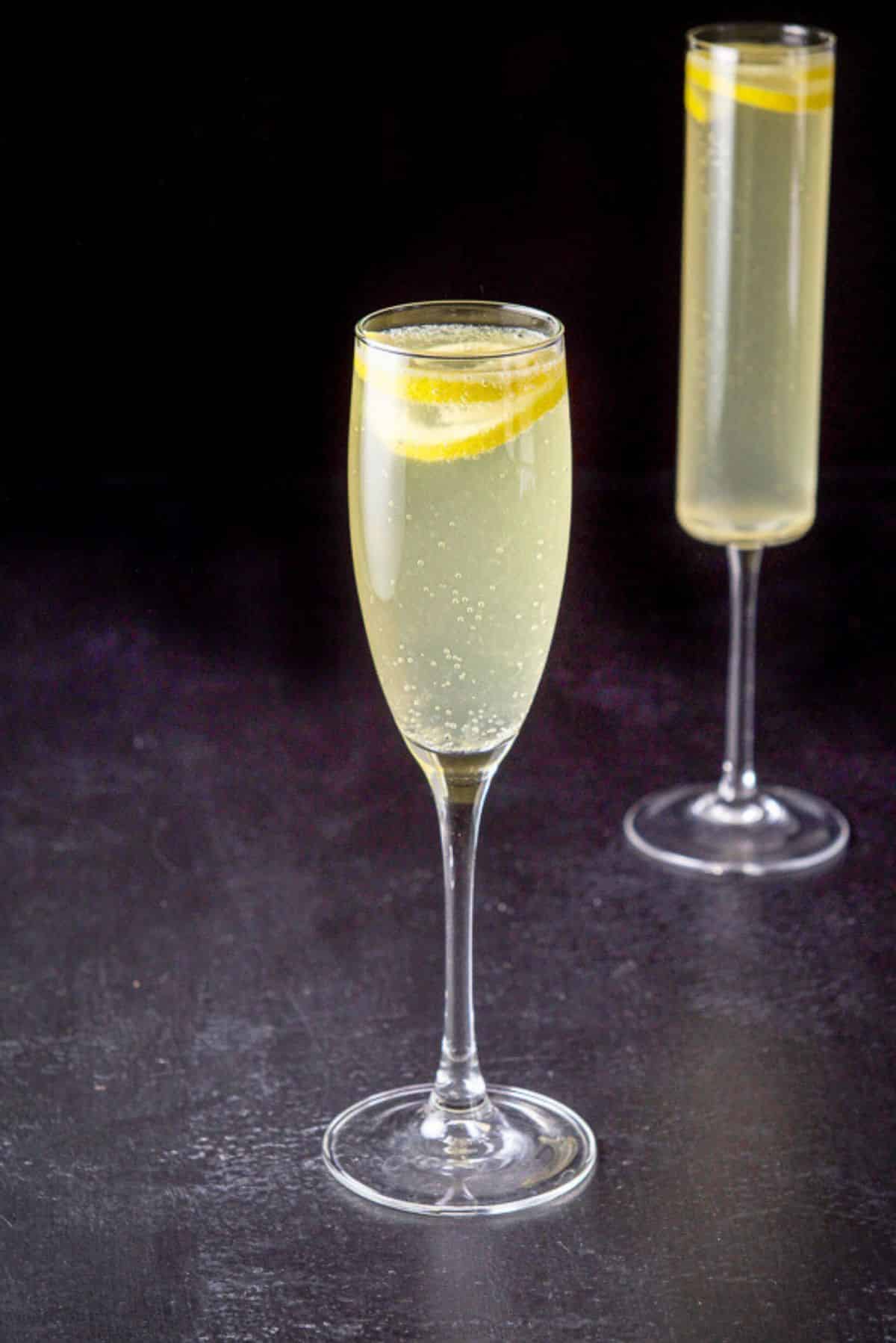 Classic champagne glass in front of the tall glass filled with the French cocktail