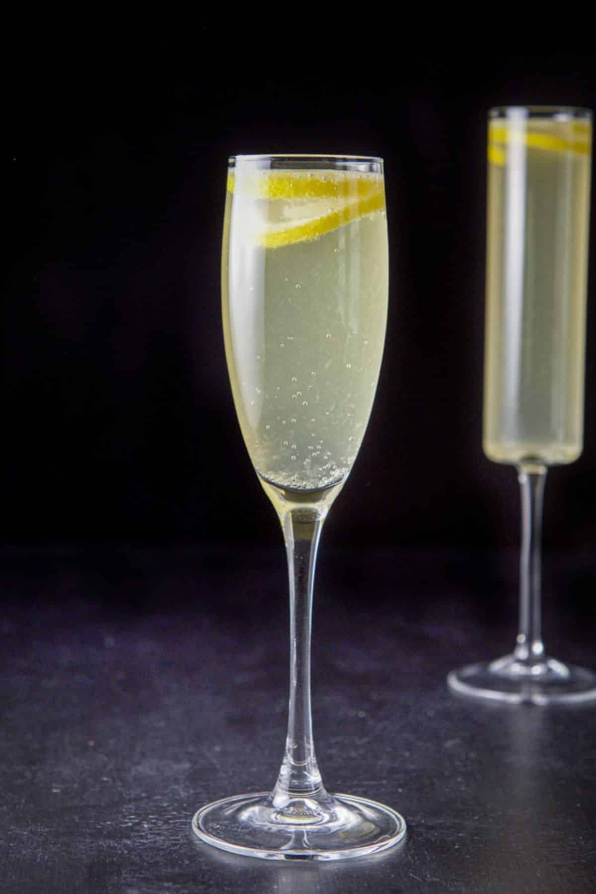 Vertical view of the classic champagne glass in front of the straight glass. You can see bubbles and the lemon twists