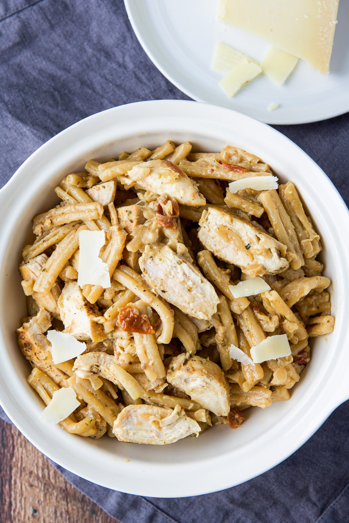 Overhead view of the bowl of pasta and chicken with a plate with cheese