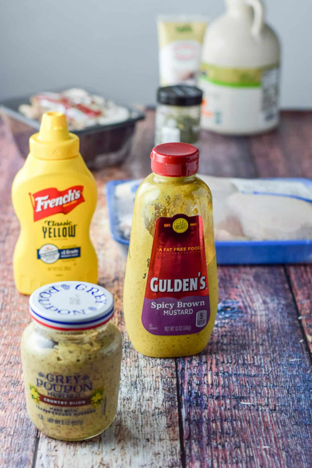 Three different mustards with mushrooms, chicken thighs, garlic and maple syrup on a wooden table