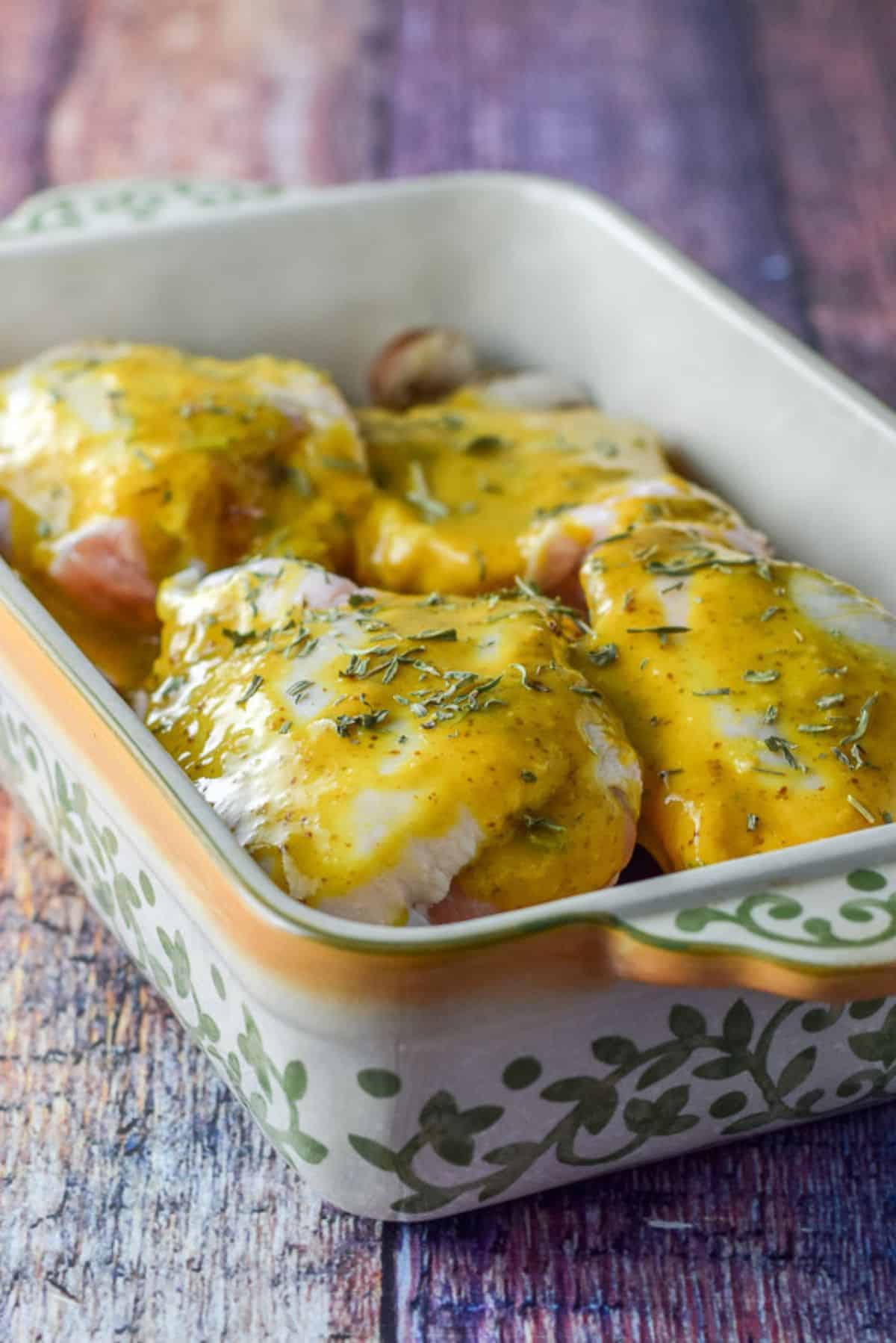 Mustard sauce poured on the chicken thighs in the baking dish