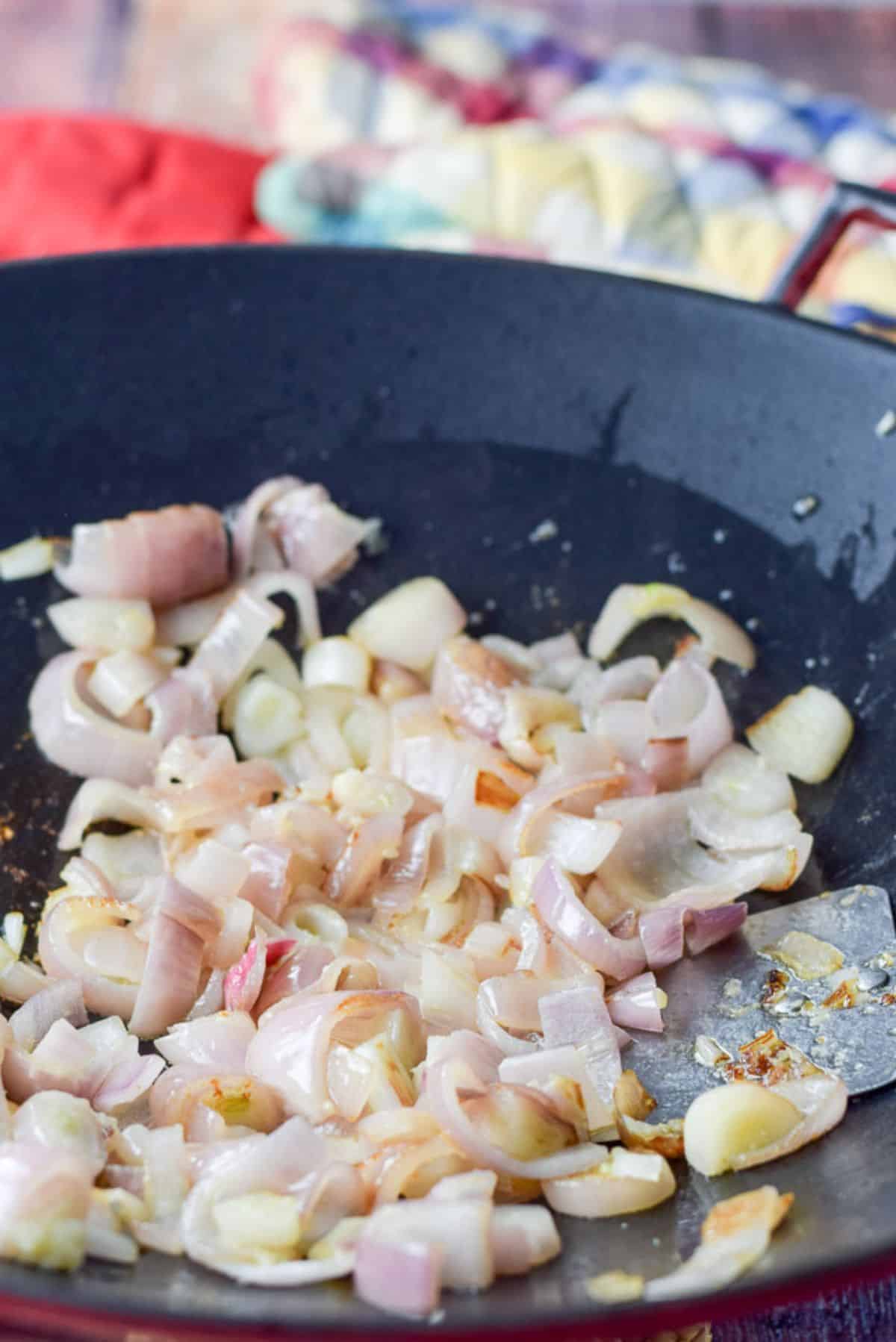 Shallots sautéd in a wok with a few oven mitts in the background