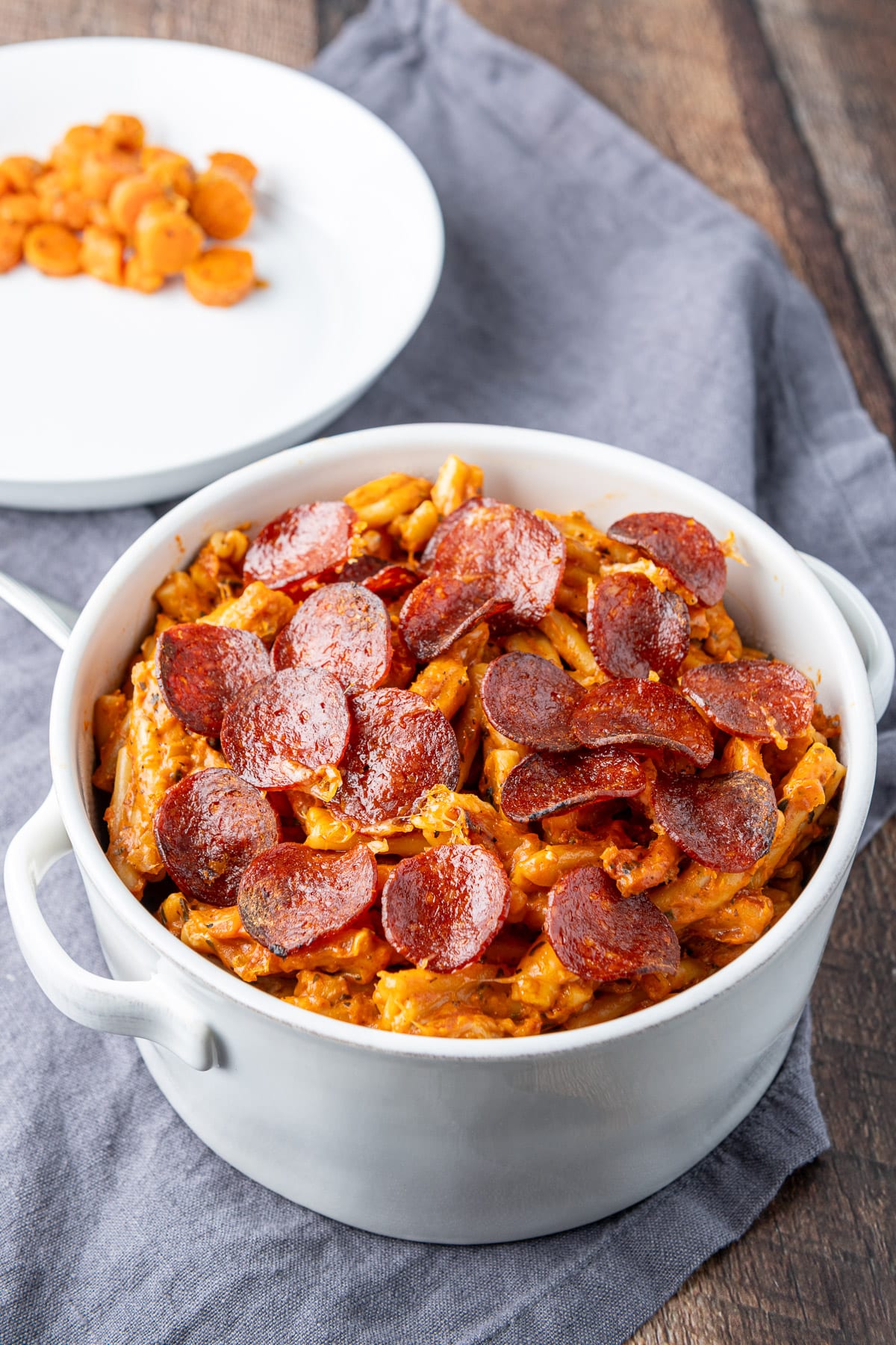 Crispy pepperoni on creamy pasta with a dish with cooked carrots on it