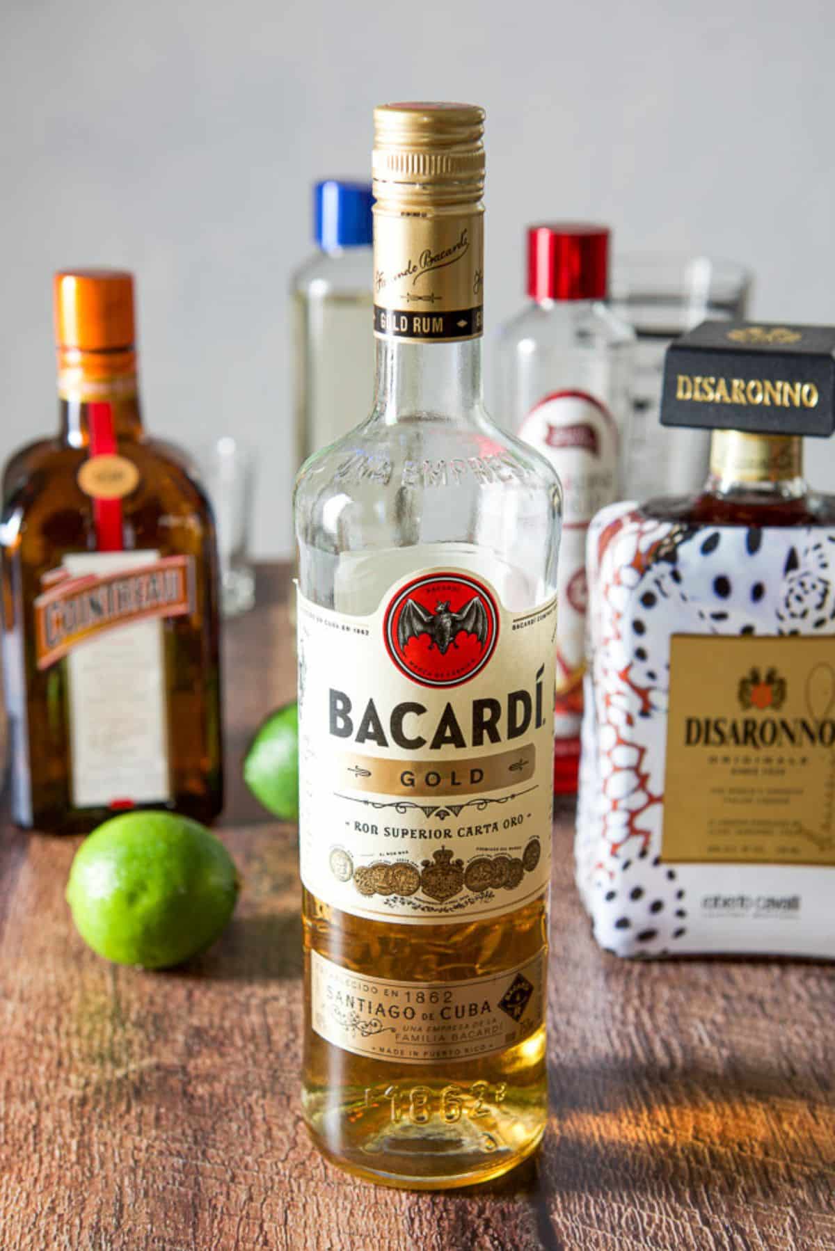 Rums, almond liquor, Cointreau, limes, simple syrup, and grenadine on a table