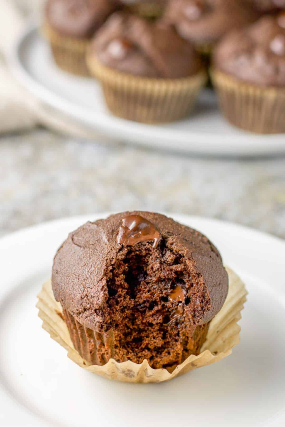 A small plate with a muffin on it with the baking cup loosened and a bite taken out of the gooey muffin