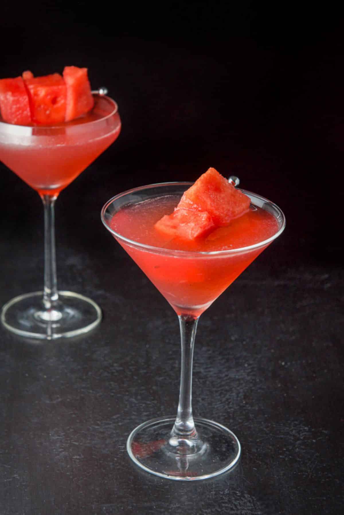A classic martini glass and a fluted glass filled with a cosmo with watermelon chunks as garnish