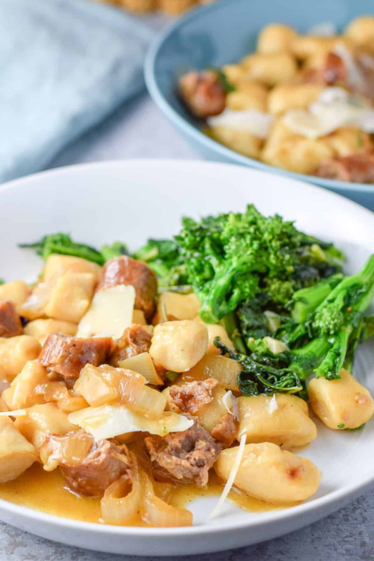 A white and blue deep plate filled with gnocchi, sauce and parmesan cheese with a side of broccoli rabe