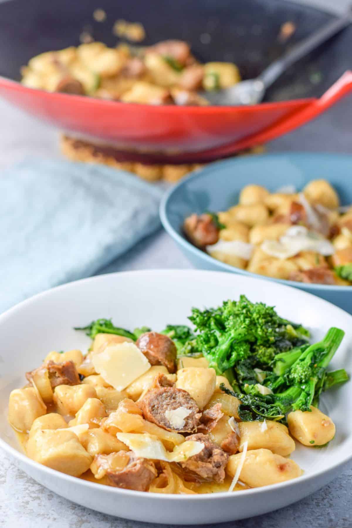 A white deep plate and blue plate with the gnocchi in it with the wok in the background