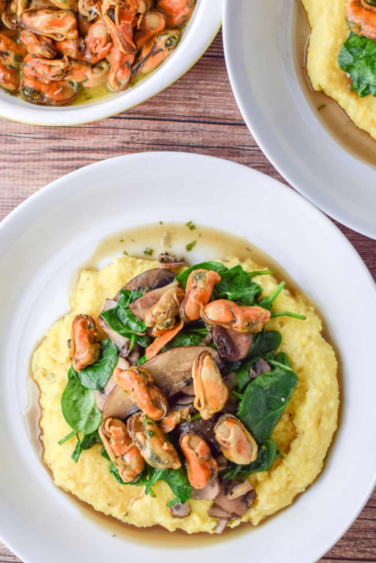 Overhead view of the white plate with mussels, sauce, veggies and polenta with a bowl of mussels in a separate dish