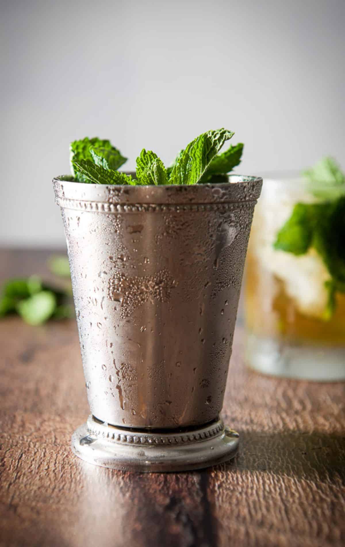 Vertical view of the metal cup and glass filled with the drink with mint sticking out of it
